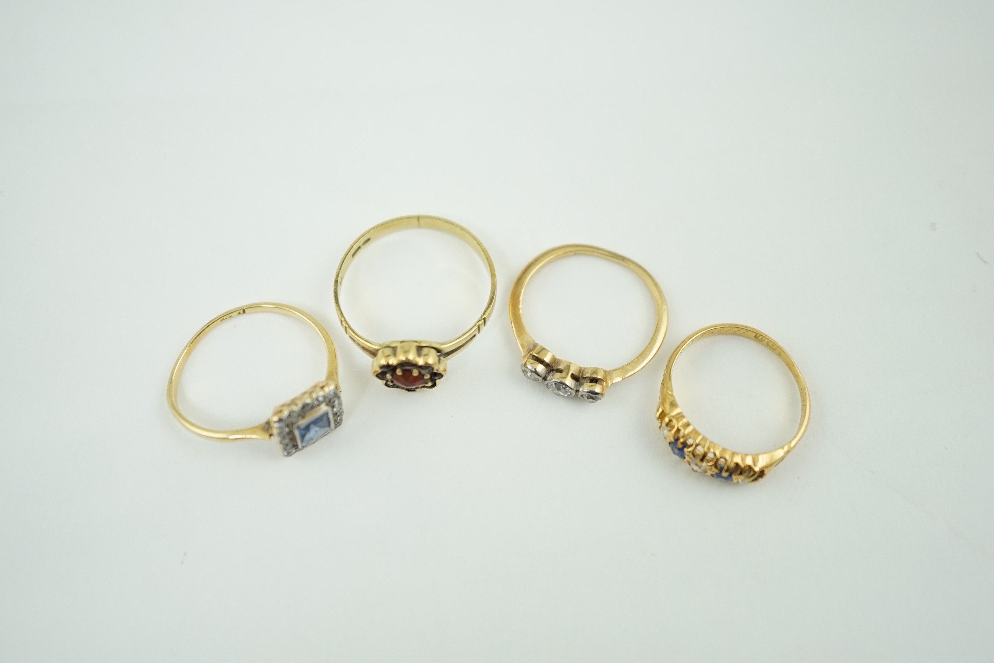 Four assorted rings including an 18ct gold, sapphire and diamond cluster set tablet ring, an 18ct sapphire and diamond half hoop, a gold and three stone diamond and a 14k gold and garnet cluster ring